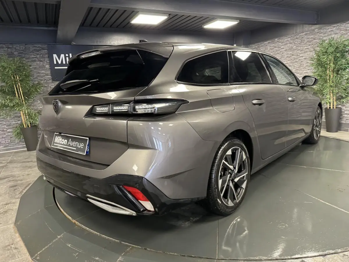 Vue 3/4 arrière droit d'une Peugeot 308 SW gris métallisé avec jantes alliage et feux arrière LED dans un showroom.