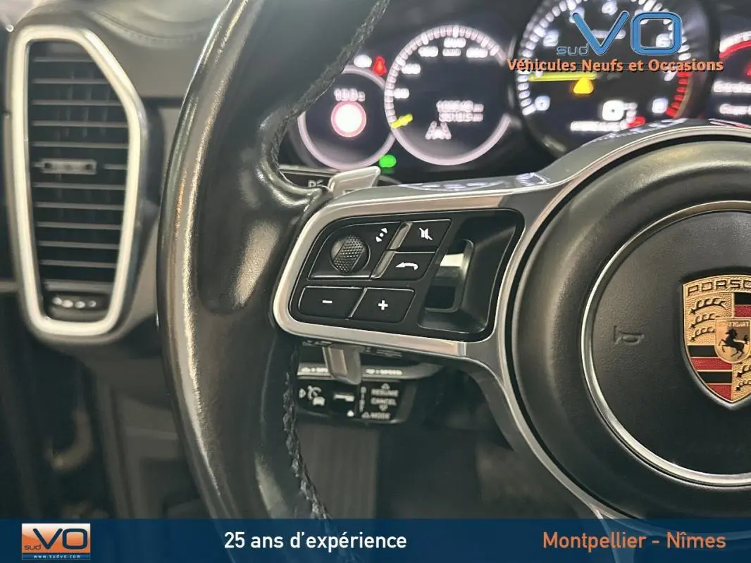 Gros plan sur le volant sport noir de la Porsche Cayenne E-Hybrid 2018 avec commandes intégrées et tableau de bord lumineux.