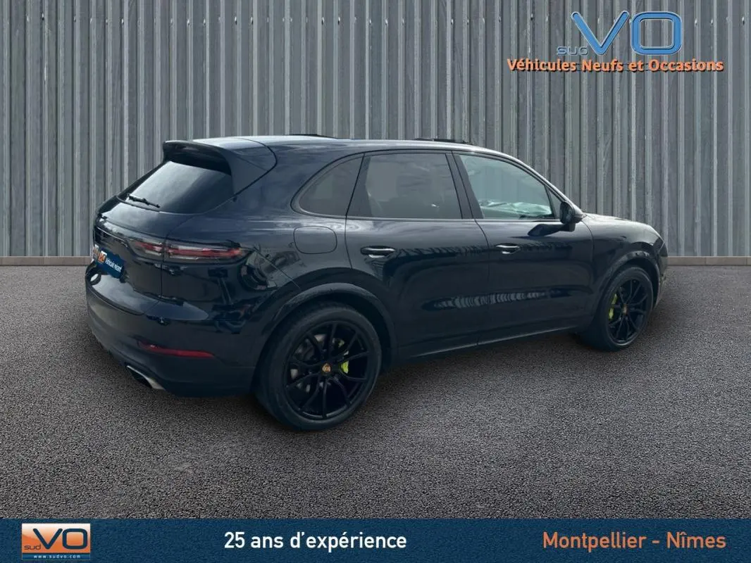 Vue 3/4 arrière droite d'un Porsche Cayenne noir avec jantes noires et feux arrière LED, stationné sur sol gris.