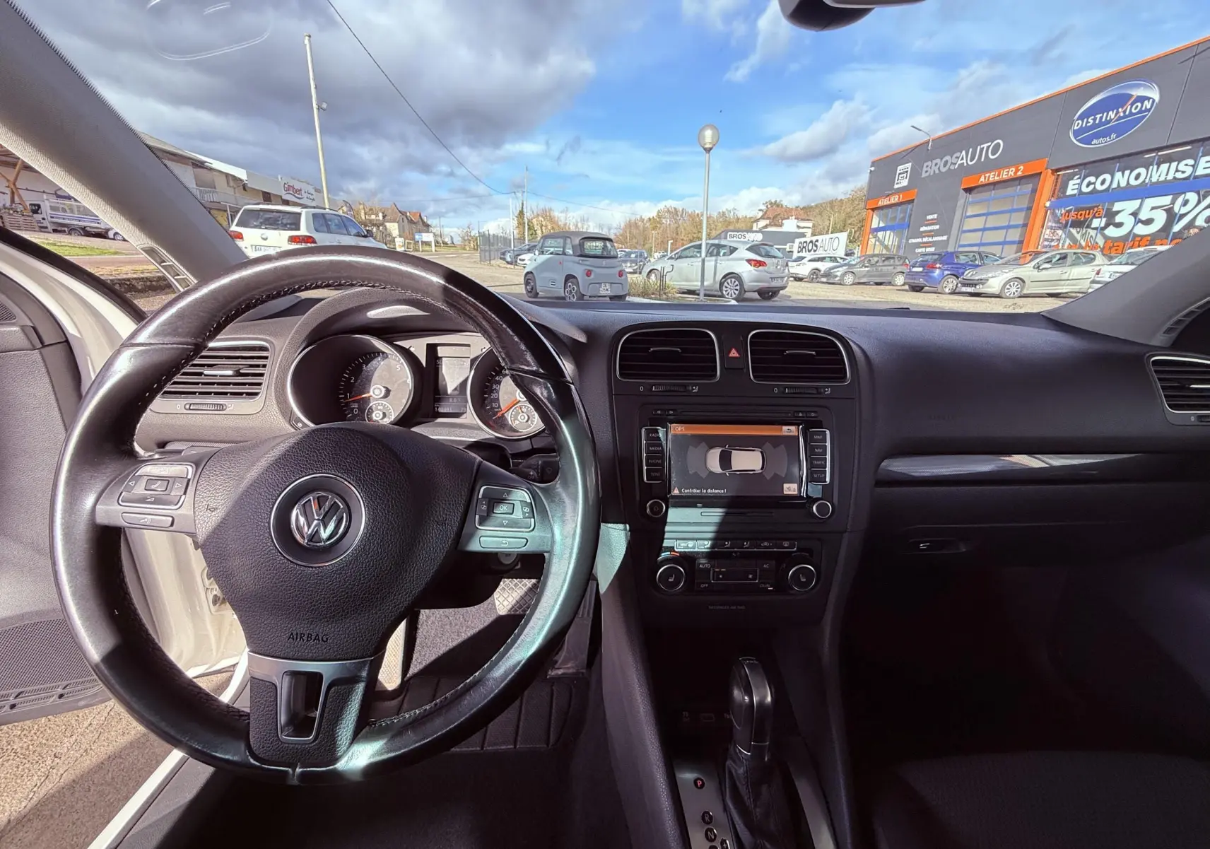 Vue intérieure du volant et tableau de bord d'une Volkswagen Golf blanche de 2012 avec boîte automatique et écran central allumé.