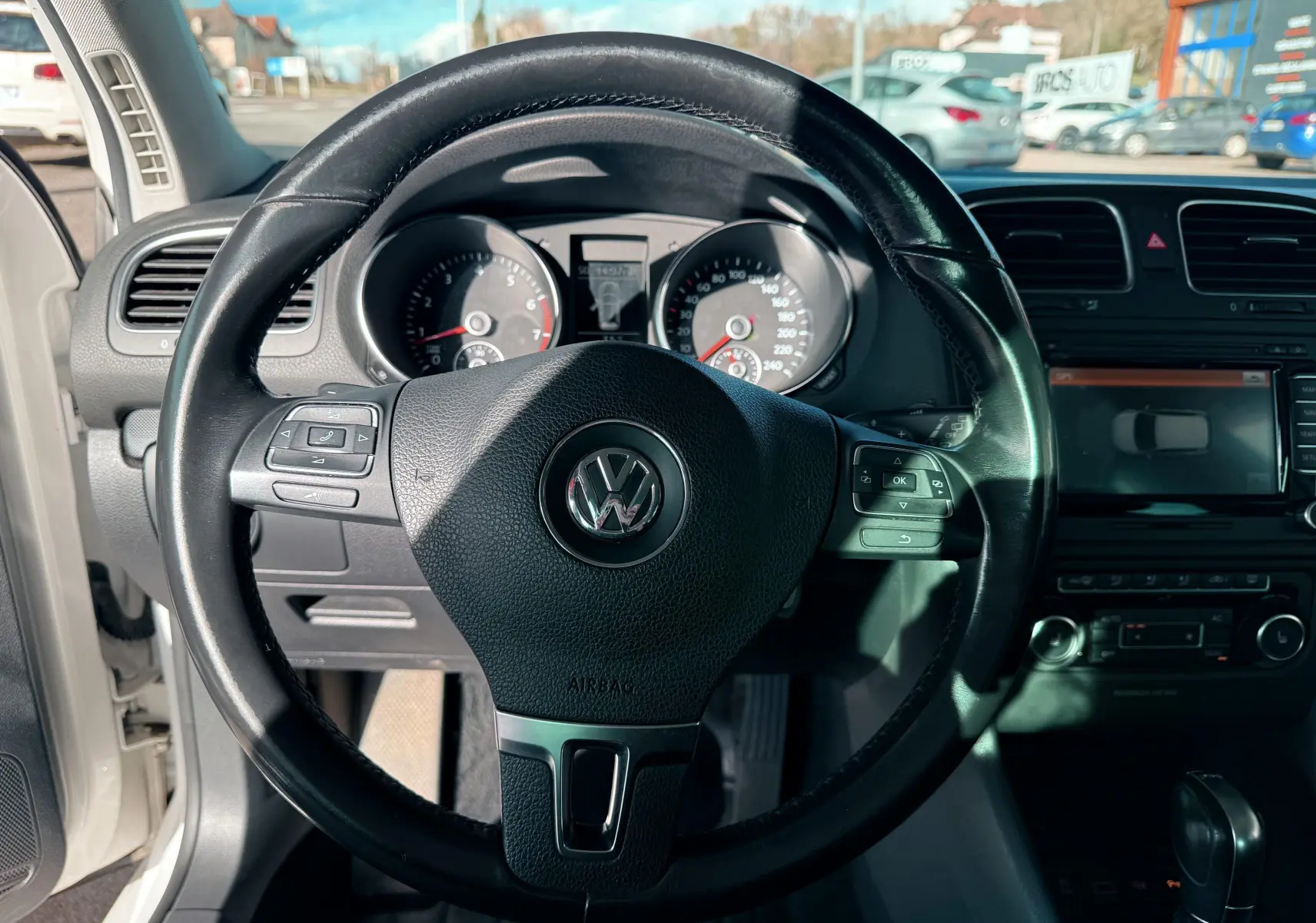 Vue rapprochée du volant en cuir noir d'une Volkswagen Golf blanche de 2012 avec tableau de bord et écran tactile visibles.