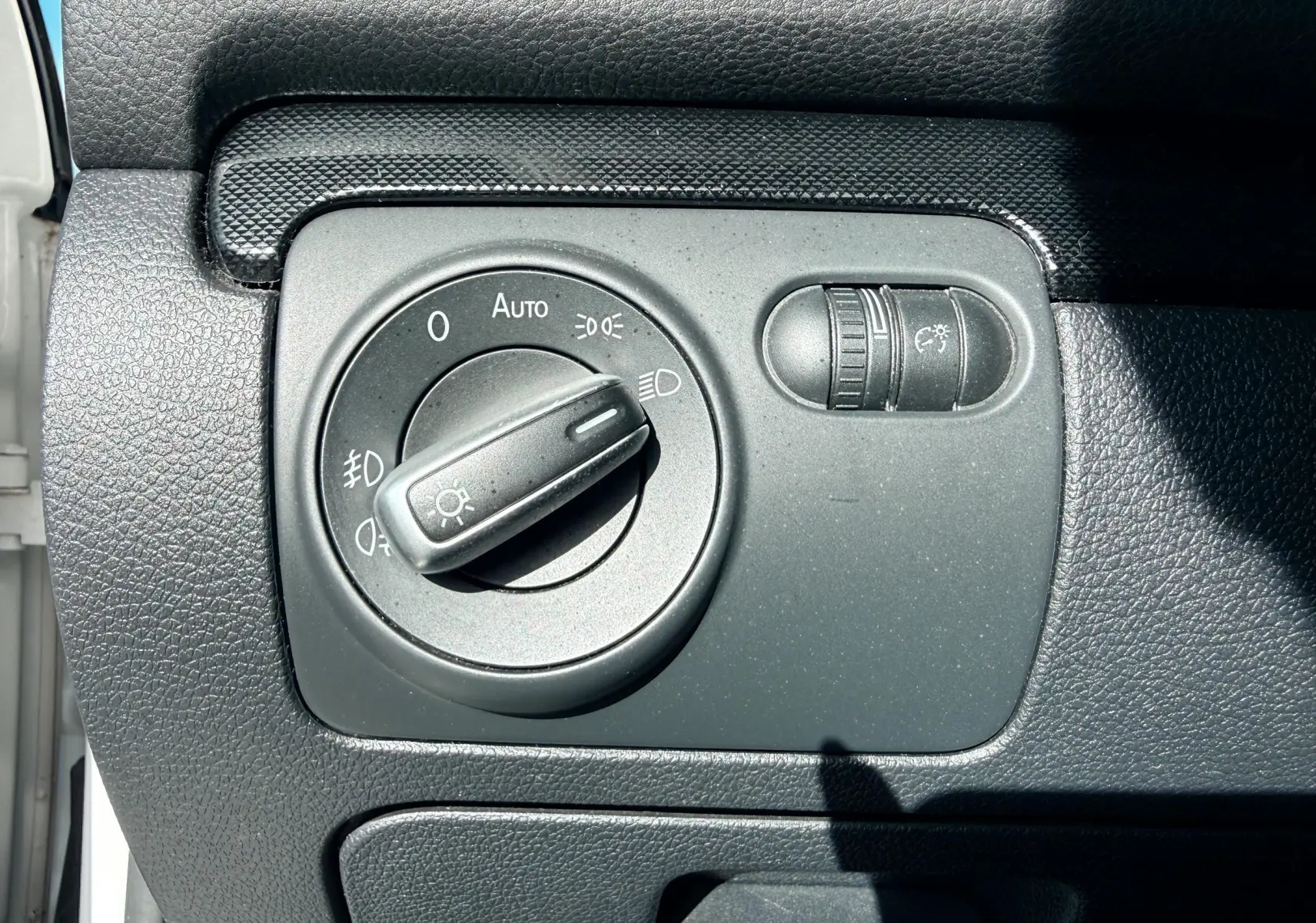 Gros plan sur le bouton de commande des phares dans l'habitacle d'une Volkswagen Golf blanche de 2012.