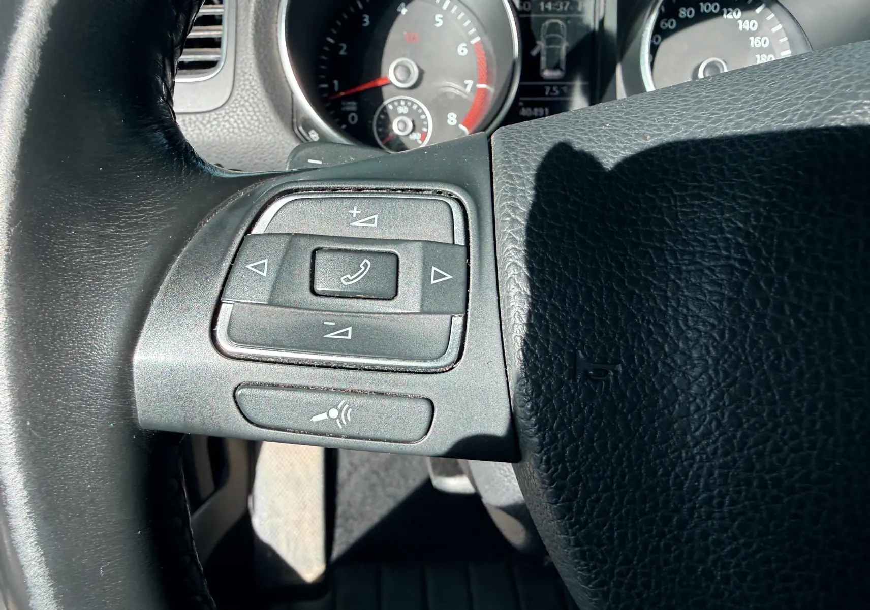 Gros plan sur les commandes du volant à gauche d'une Volkswagen Golf blanche, avec tableau de bord en arrière-plan.