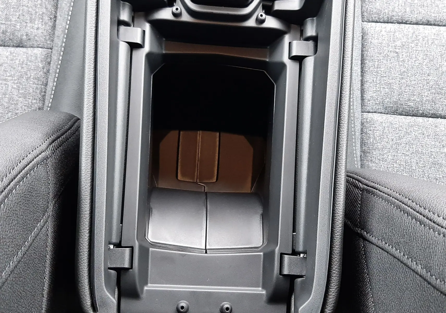 Vue rapprochée de l'accoudoir central ouvert du Renault Austral Ph.2 gris schiste, montrant le rangement intérieur et les sièges en tissu gris.