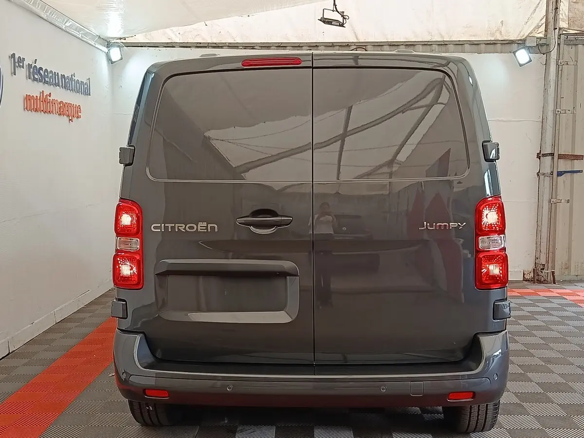 Vue arrière du Citroën Jumpy gris foncé 2025 avec portes battantes et feux arrière allumés dans un garage.