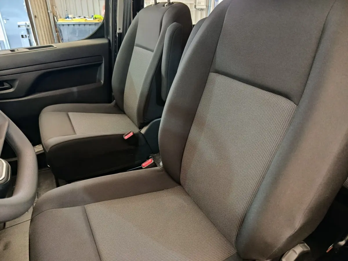Vue intérieure côté conducteur du Citroën Jumpy gris foncé, montrant les sièges avant en tissu noir et gris.