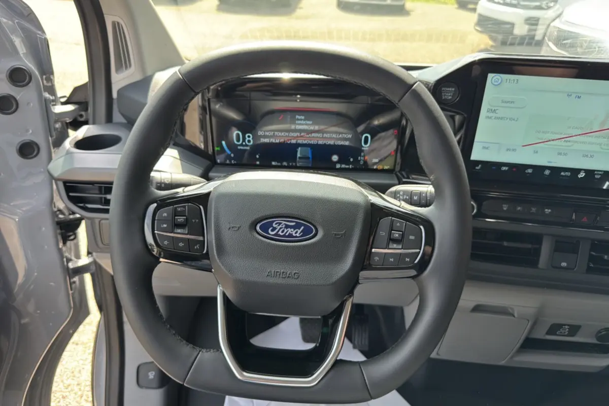 Vue intérieure centrée sur le volant multifonctions noir du Ford Transit Custom 2026, avec tableau de bord numérique et écran tactile.