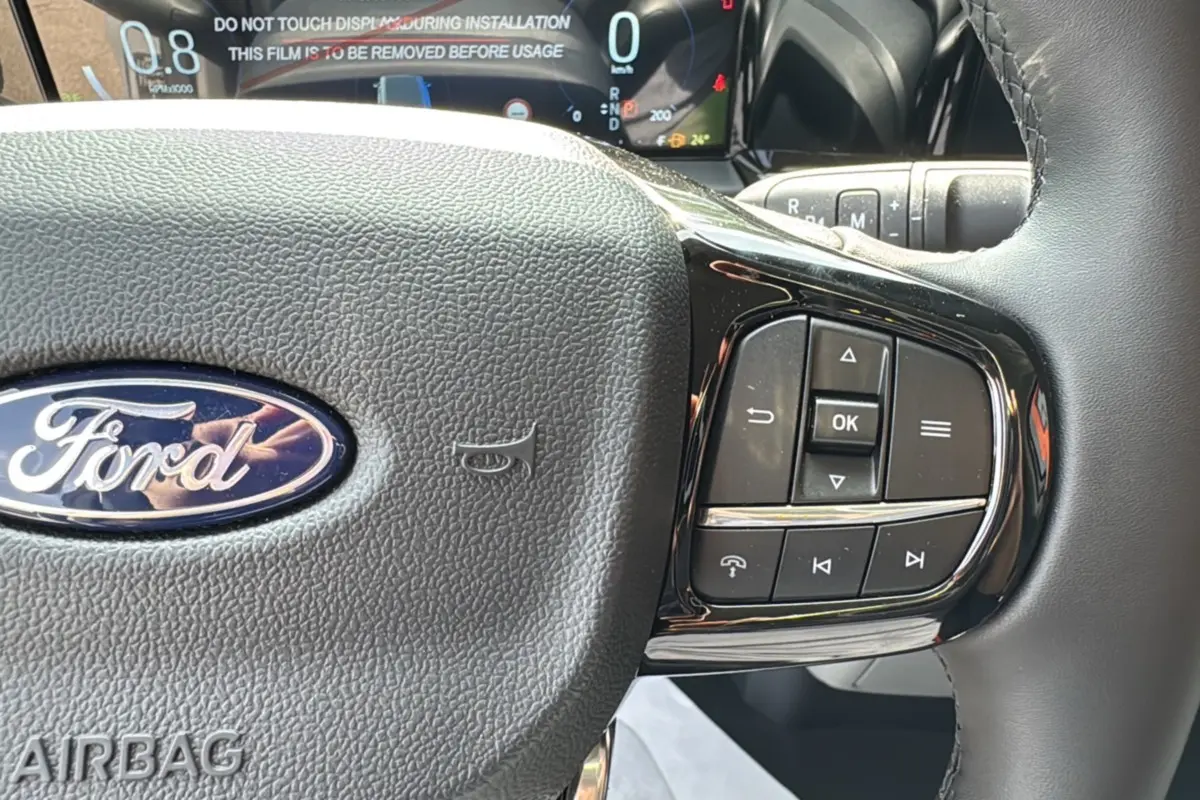 Gros plan sur le volant noir du Ford Transit Fourgon Custom 2026 avec commandes multifonctions et tableau de bord numérique.