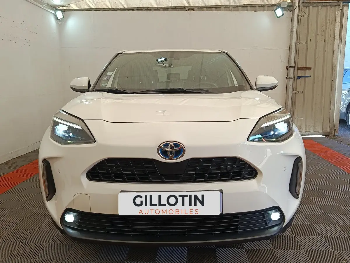 Vue de face du Toyota Yaris Cross blanc avec phares LED allumés et calandre noire distinctive.