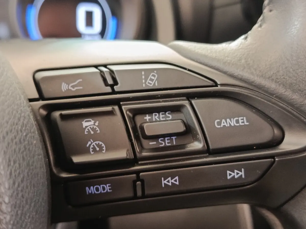 Gros plan sur les commandes au volant du Toyota Yaris Cross 1.5 Hybrid blanc, avec régulateur adaptatif et aide au maintien de voie.