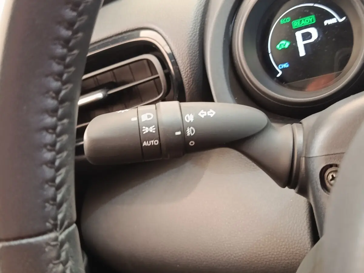 Gros plan sur la manette de commande des phares et clignotants côté gauche du tableau de bord noir d'une Toyota Yaris Cross hybride.