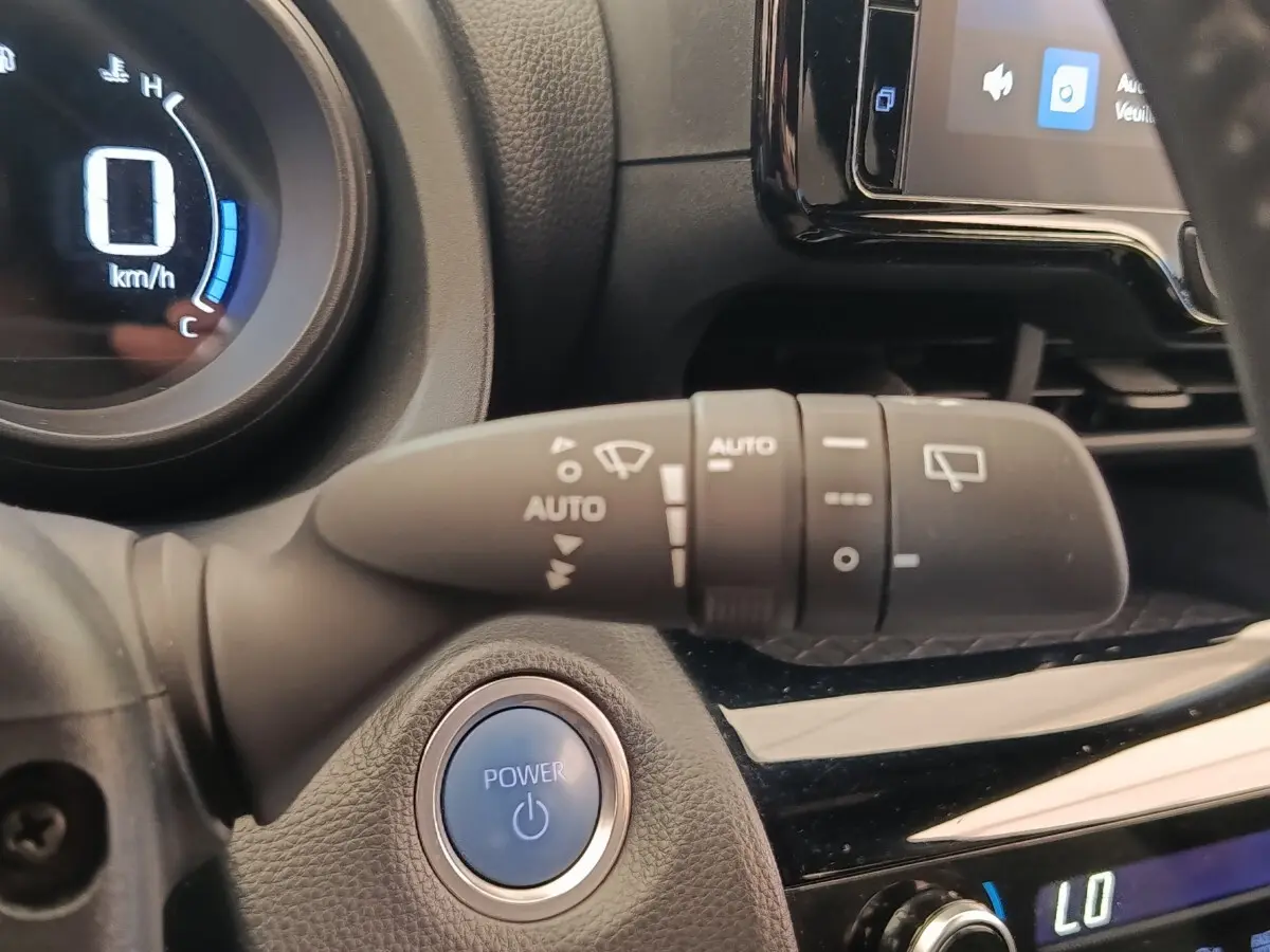 Gros plan sur le bouton démarrage bleu POWER et la commande d’essuie-glace dans l’habitacle noir de la Toyota Yaris Cross.