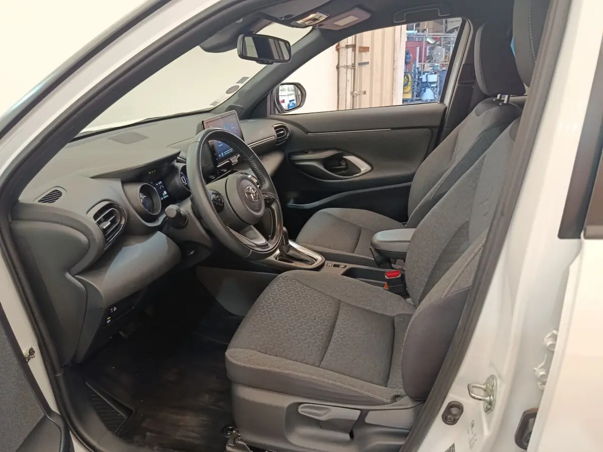 Intérieur côté conducteur d'une Toyota Yaris Cross blanche, sièges gris et tableau de bord avec écran tactile.