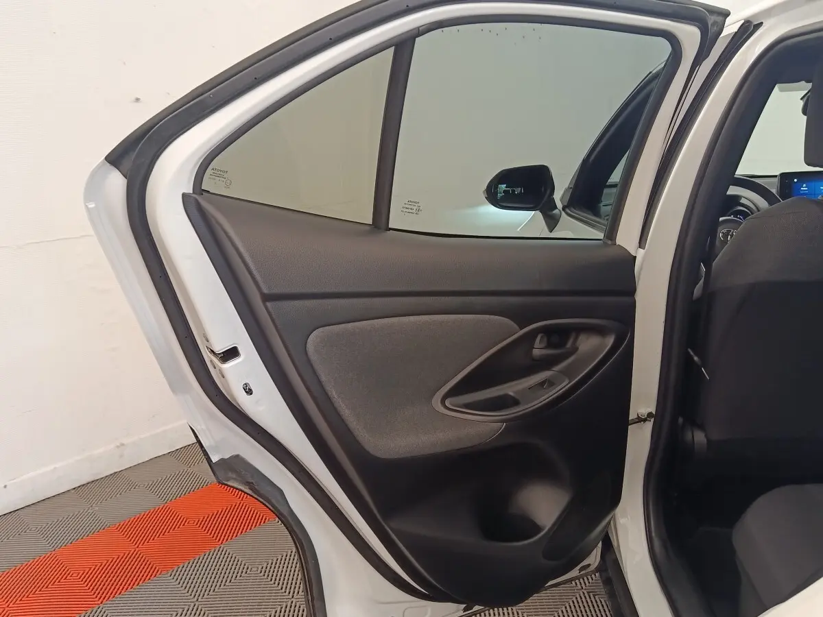 Vue intérieure de la porte arrière gauche ouverte d'une Toyota Yaris Cross blanche, avec garniture noire et grise.