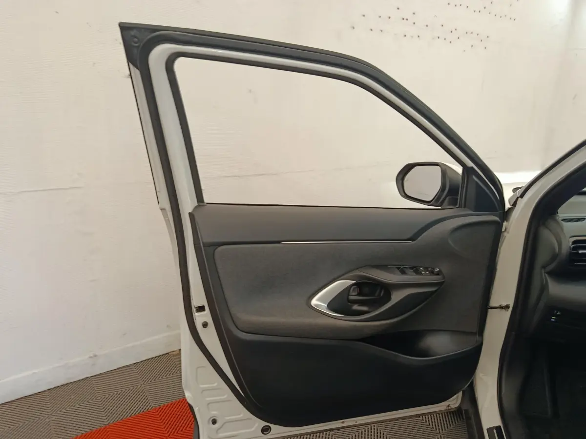 Vue intérieure de la porte avant droite blanche d'une Toyota Yaris Cross 1.5 Hybrid 2022 avec garniture noire et commandes.