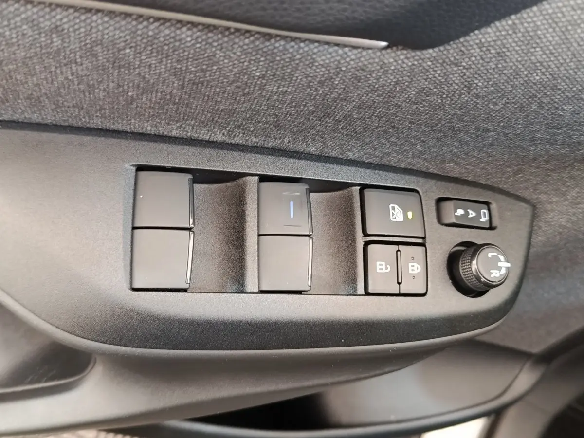 Gros plan sur les commandes de porte côté conducteur de la Toyota Yaris Cross blanche, avec boutons de vitres et réglage rétroviseurs.
