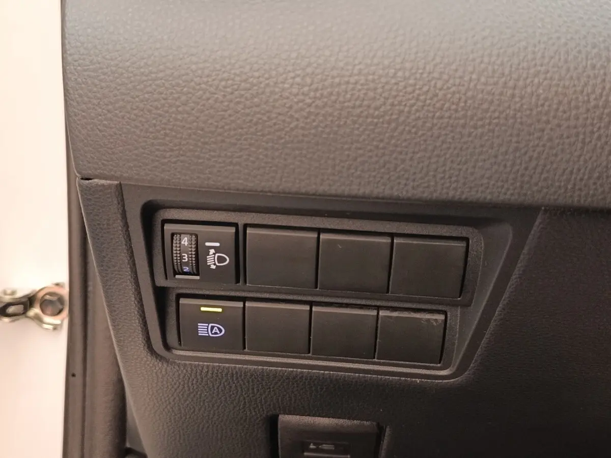 Gros plan sur les commandes d’éclairage côté gauche d’une Toyota Yaris Cross blanche, intérieur noir.