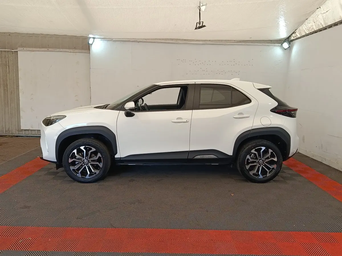 Profil droit d'un Toyota Yaris Cross blanc 2022 avec jantes alliage noires et détails noirs contrastants sous un éclairage intérieur.