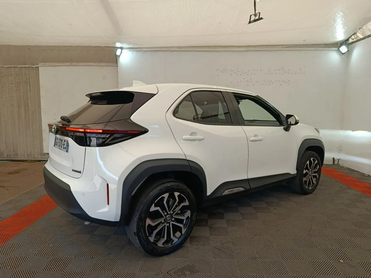 Vue 3/4 arrière droite d'une Toyota Yaris Cross blanche avec toit noir et jantes alliage bicolores dans un garage.