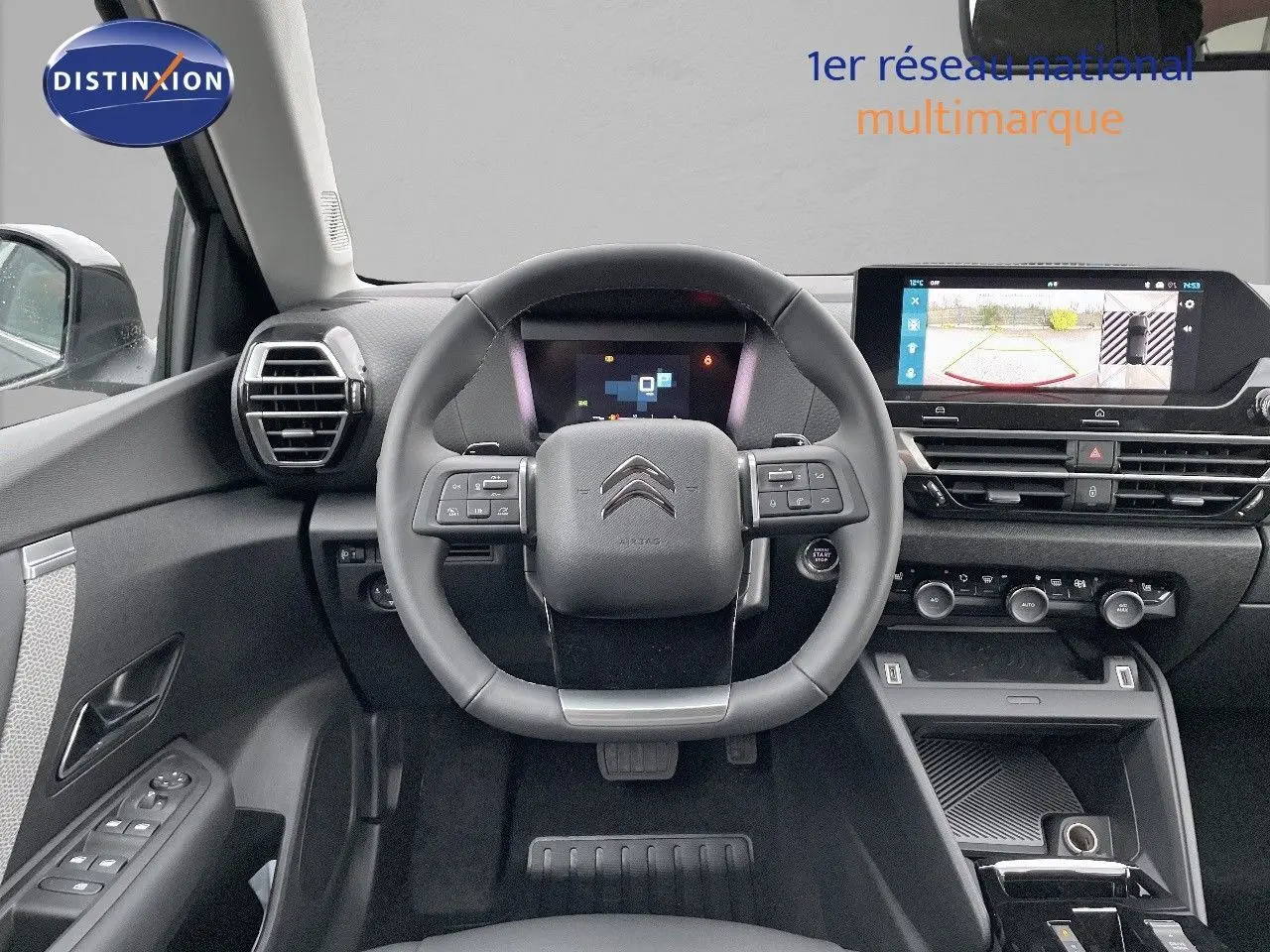 Vue intérieure du poste de conduite d'une Citroën C4 gris platinium, avec volant multifonction et écran tactile affichant la caméra de recul.