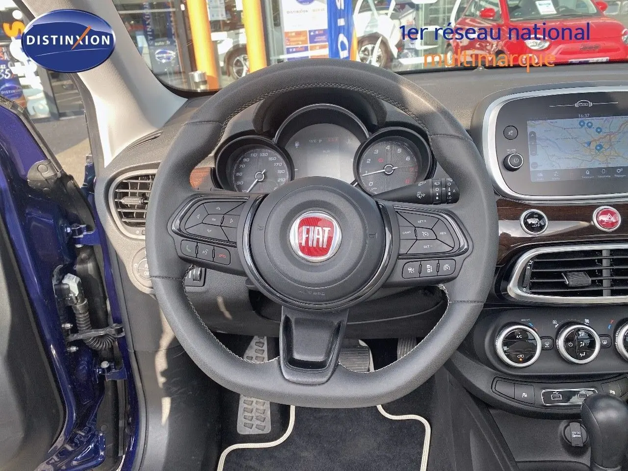 Vue intérieure centrée sur le volant du Fiat 500X bleu Venezia Metal avec tableau de bord et écran tactile visible.