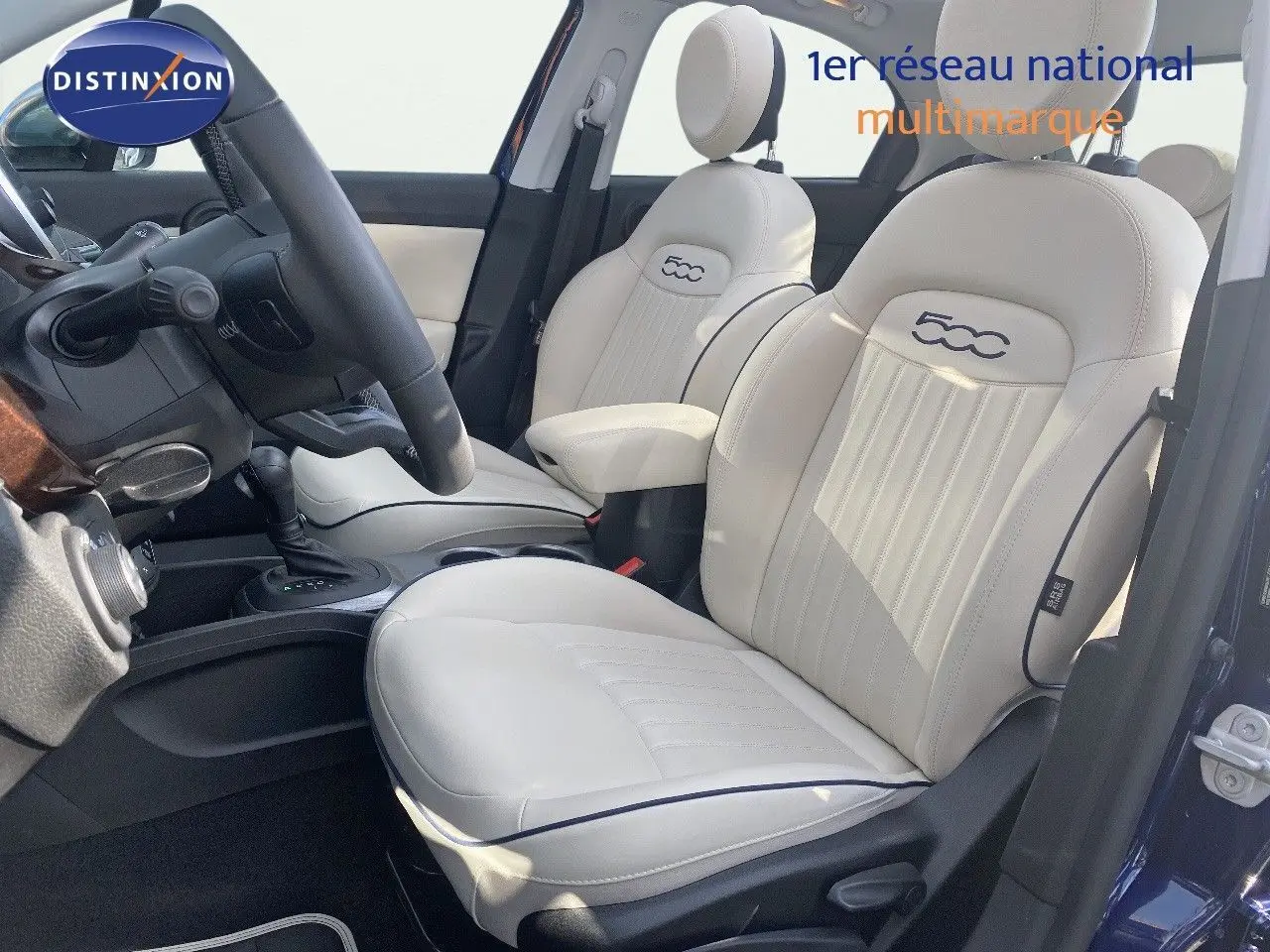 Intérieur de la Fiat 500X 2021 en cuir ivoire, vue côté gauche sur les sièges avant et le volant, ambiance lumineuse naturelle.