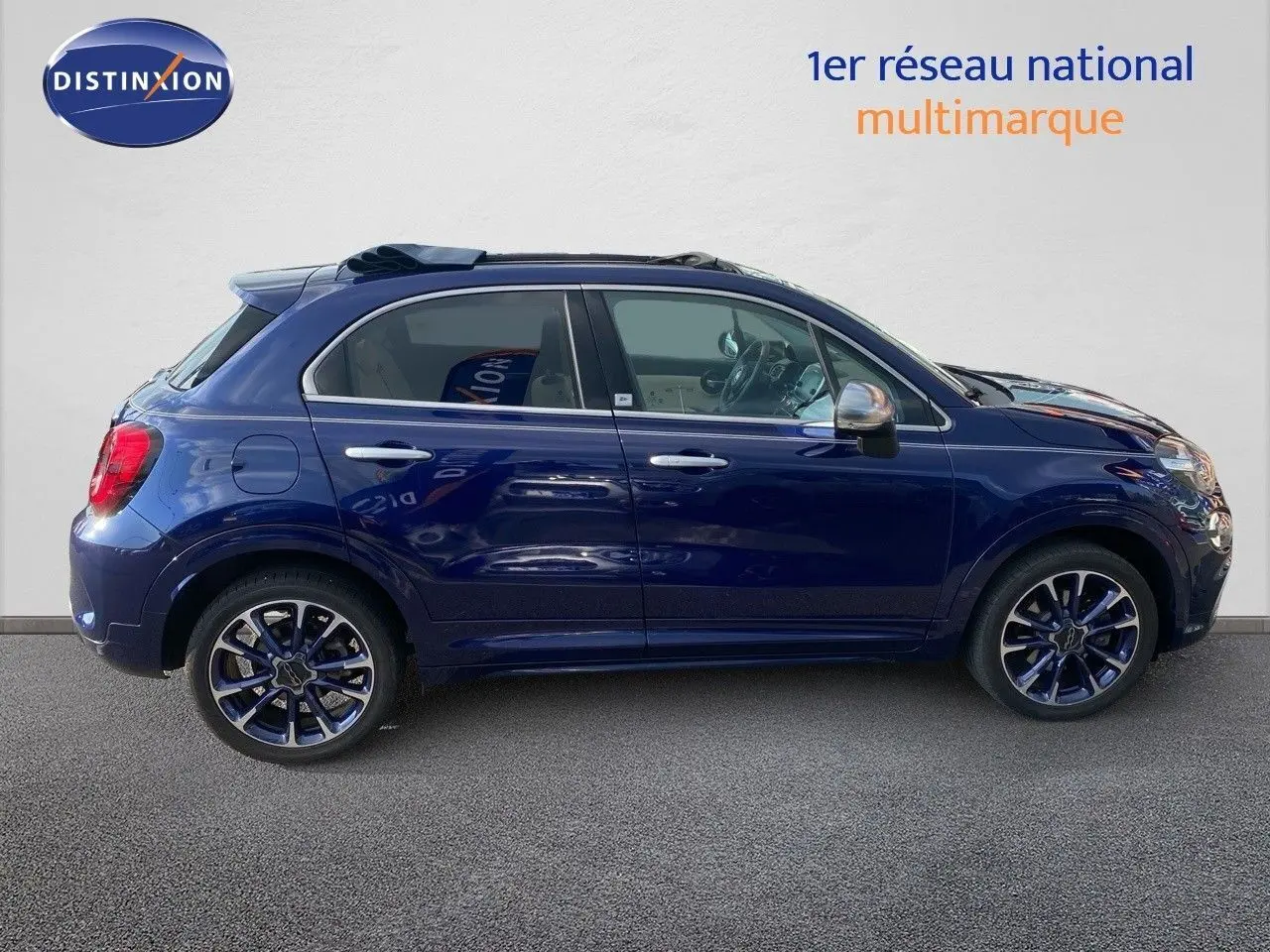 Profil côté gauche d'une Fiat 500X bleu Venezia métal avec jantes bi-ton et rétroviseurs chromés, vue en extérieur.