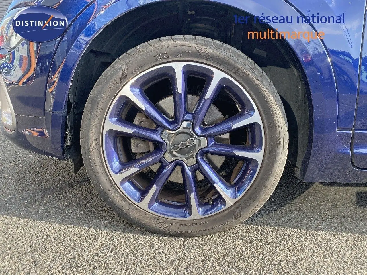 Gros plan sur la roue avant gauche d'une FIAT 500X bleu Venezia Metal avec jante alliage bicolore distinctive.