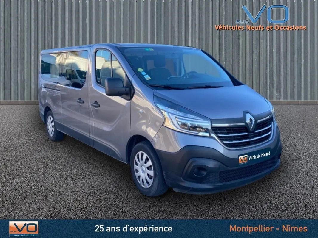 Renault Trafic Fourgon Combi gris clair vu en 3/4 avant droit avec porte latérale et vitres surteintées.