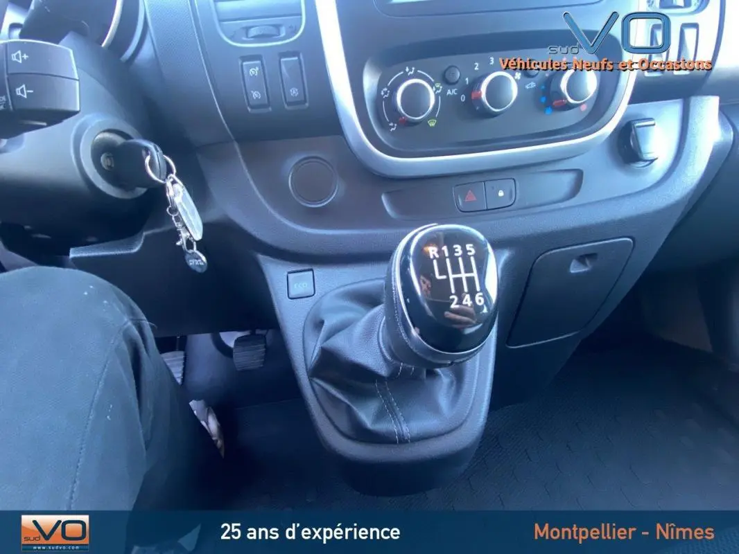 Gros plan sur le levier de vitesses manuel et le tableau de bord du Renault Trafic Fourgon gris clair de 2019.