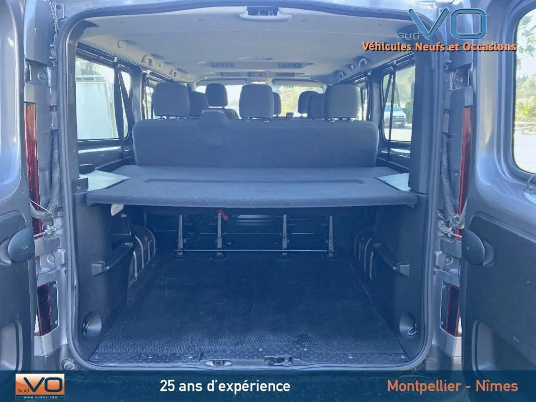 Vue arrière ouverte du Renault Trafic Combi gris clair montrant l'espace de chargement et les sièges arrière noirs.