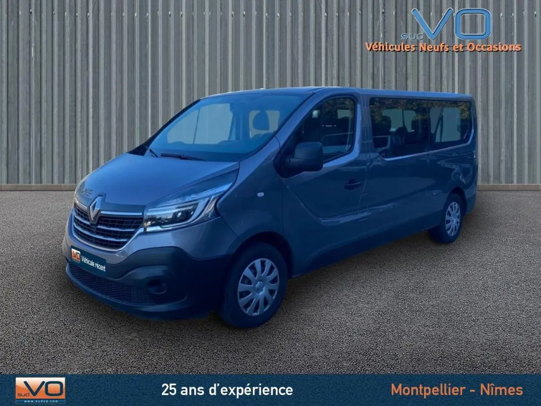 Renault Trafic Fourgon Combi gris clair vu en 3/4 avant droit avec porte latérale et vitres surteintées.