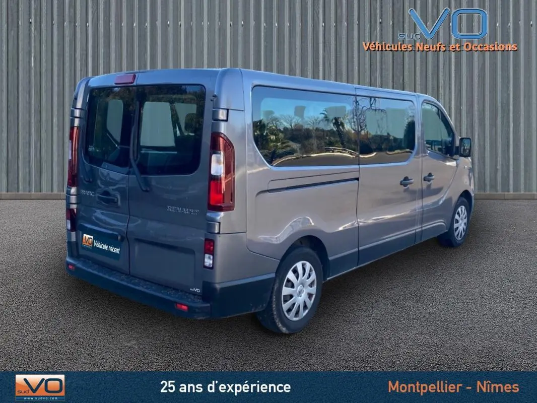 Vue 3/4 arrière droite d'un Renault Trafic Fourgon Combi gris clair avec vitres surteintées et porte latérale visible.