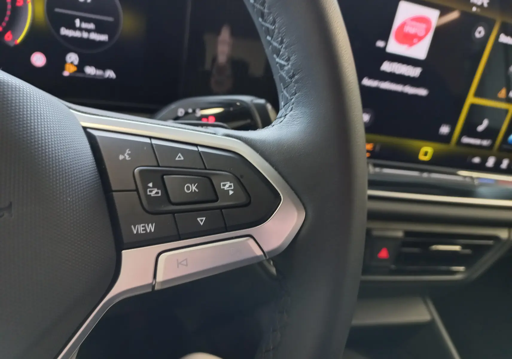 Gros plan sur les commandes au volant du Volkswagen Tiguan 2025, avec affichage numérique en arrière-plan.