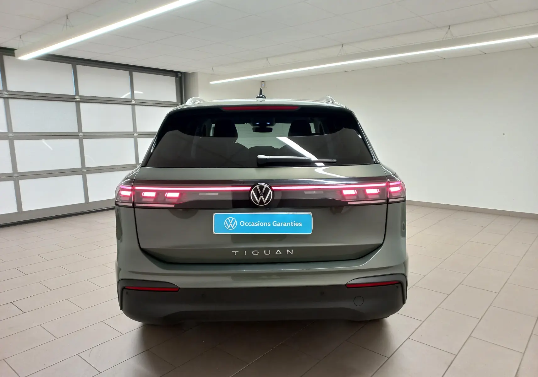 Vue arrière d'un Volkswagen Tiguan 2025 vert Cipressino avec feux LED allumés dans un showroom.
