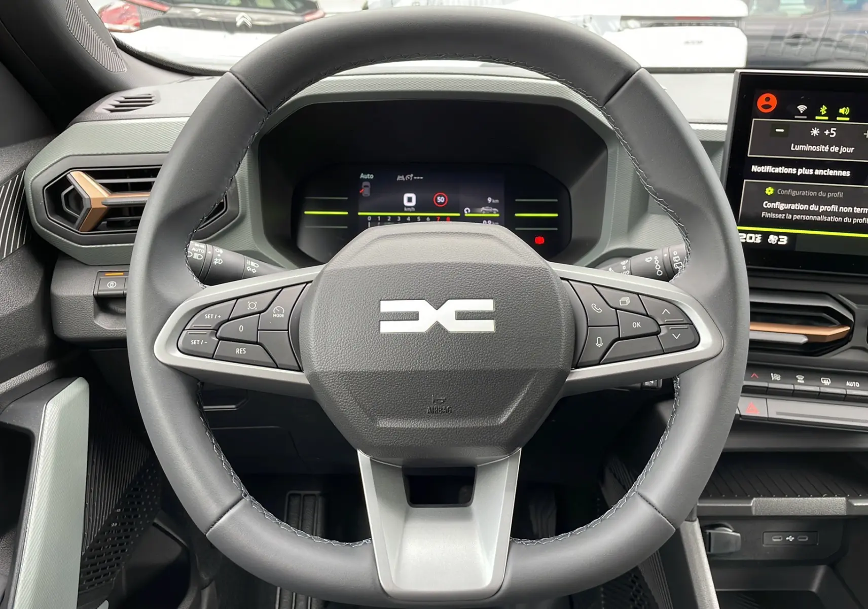 Vue intérieure centrée sur le volant cuir du Dacia Duster 2025, avec tableau de bord numérique et écran tactile visible.