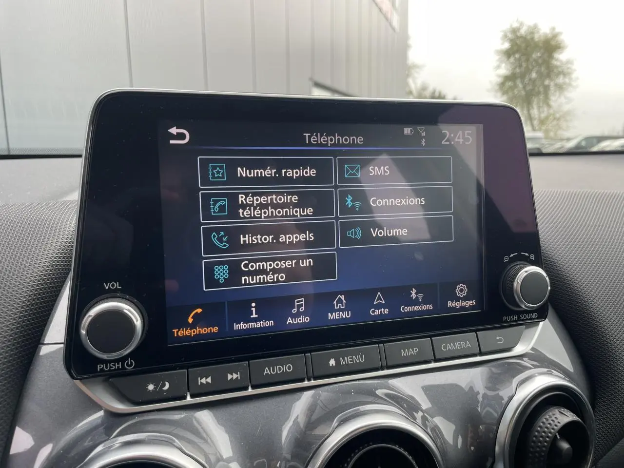 Écran tactile central du Nissan Juke 2024 gris Silver affichant le menu téléphone avec commandes physiques en dessous.