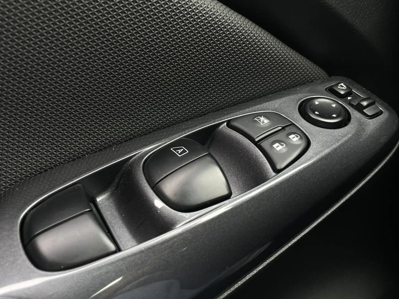 Gros plan sur les commandes de lève-vitres et rétroviseurs côté conducteur du Nissan Juke gris Silver 2024.