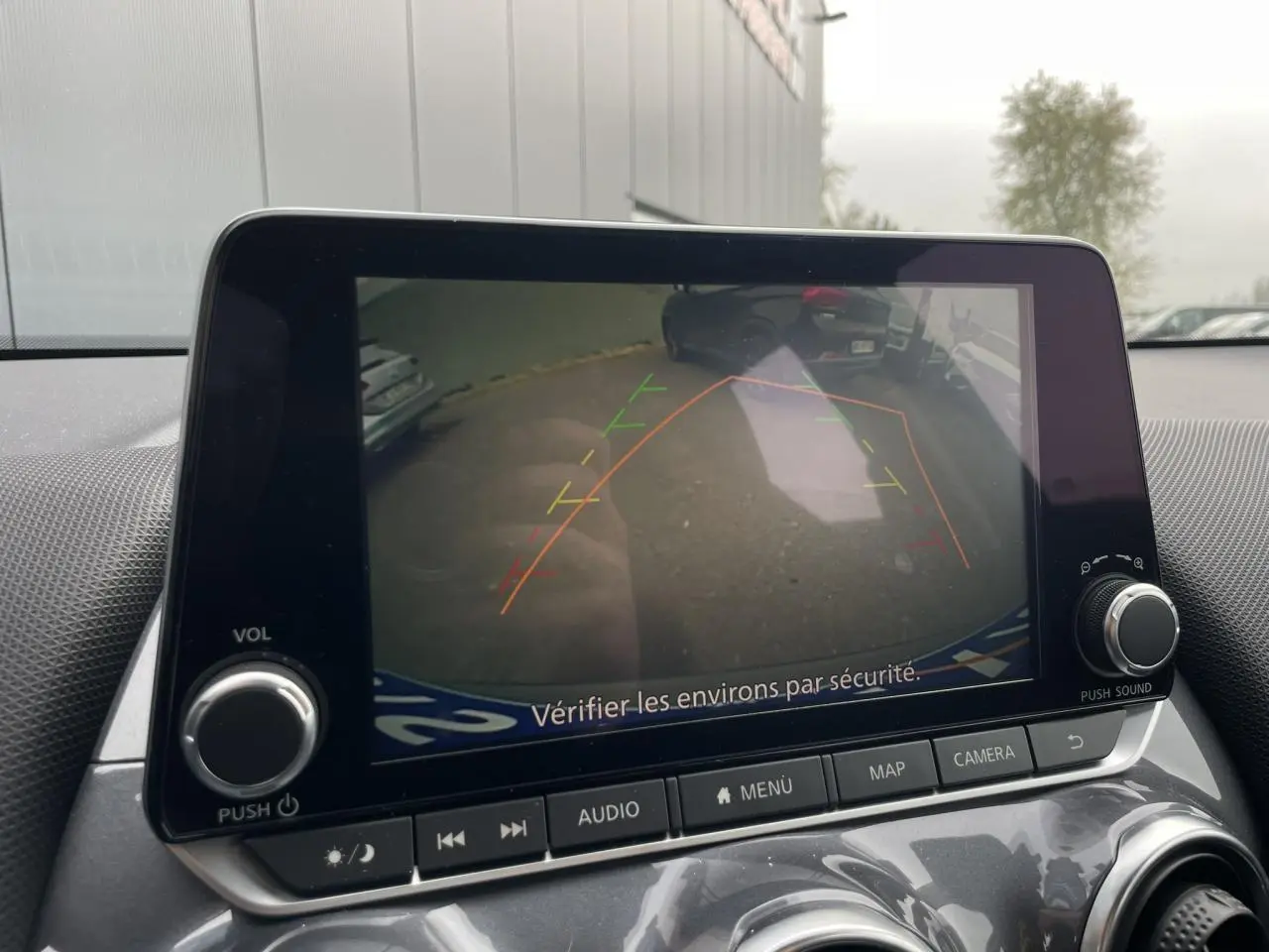 Écran tactile intérieur montrant la caméra de recul du Nissan Juke gris silver, avec les lignes d’aide au stationnement visibles.