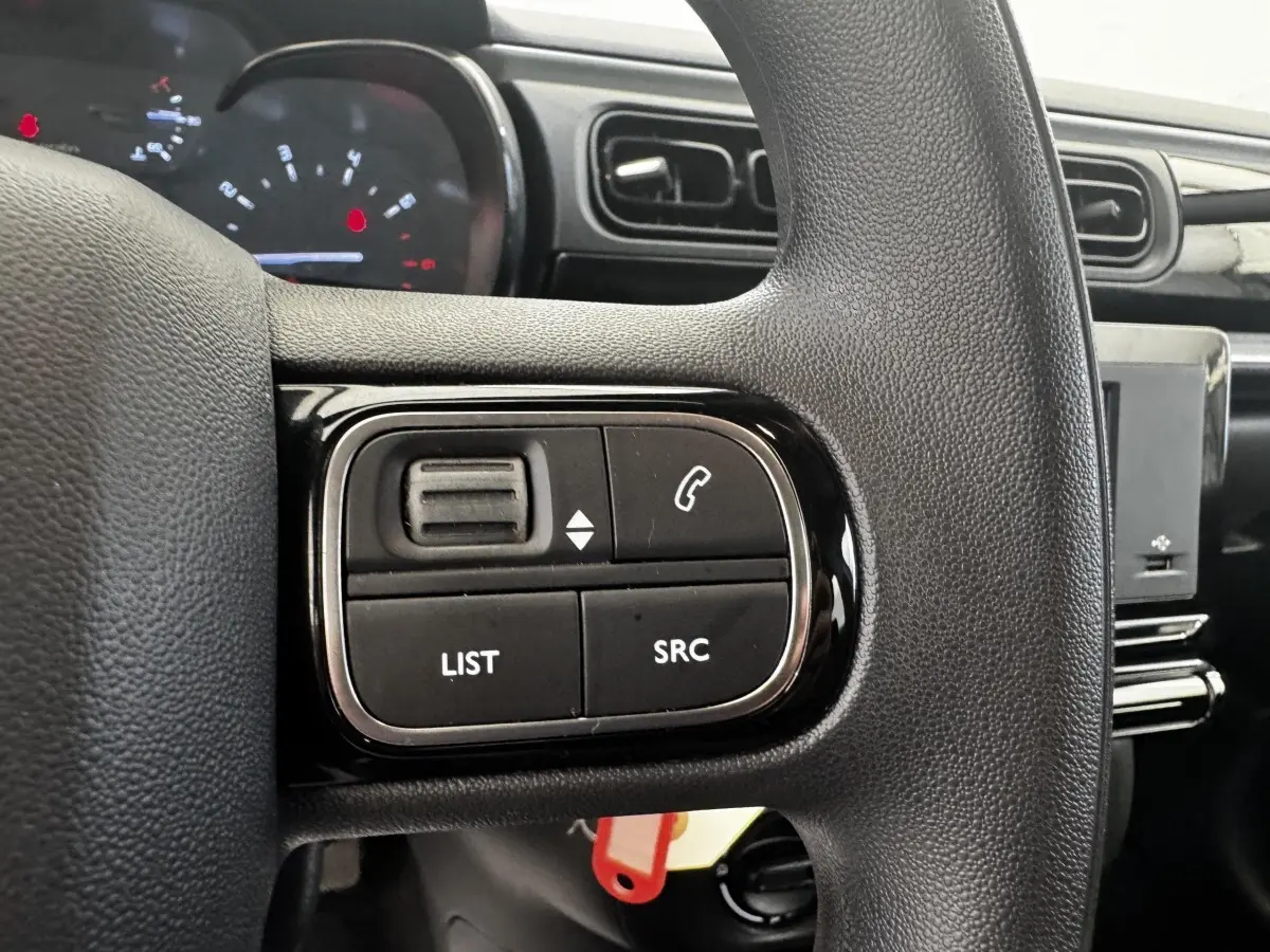 Gros plan sur les commandes du volant noir de la Citroën C3 beige, avec tableau de bord et écran tactile en arrière-plan.