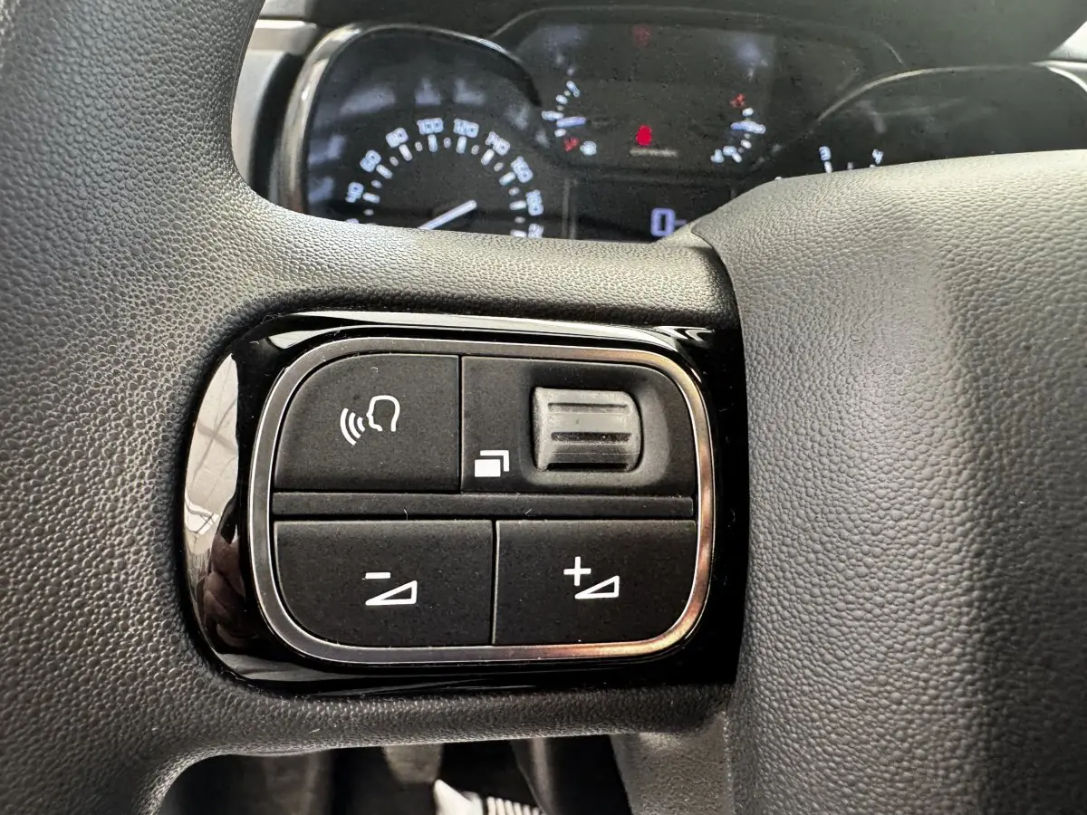Gros plan sur les commandes du volant noir de la Citroën C3 beige PureTech 83, avec tableau de bord en arrière-plan flou.