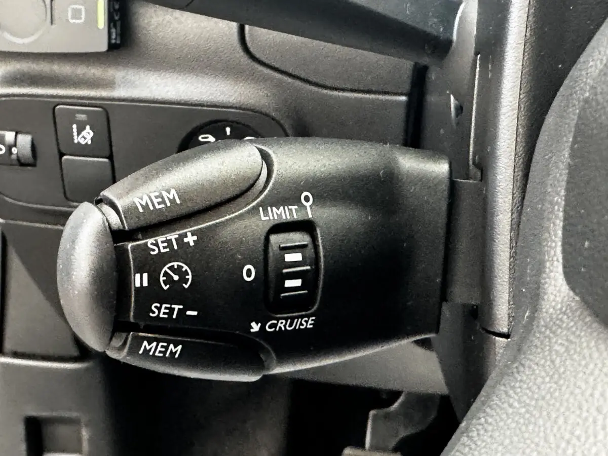 Gros plan sur la commande de régulateur de vitesse au volant d'une Citroën C3 beige, version PureTech 83 S&S BVM Feel.