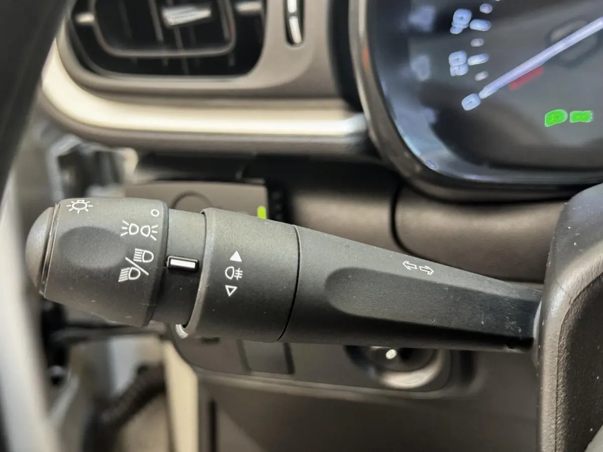 Gros plan sur la commande des phares et clignotants à gauche du volant d’une Citroën C3 beige, tableau de bord partiellement visible.