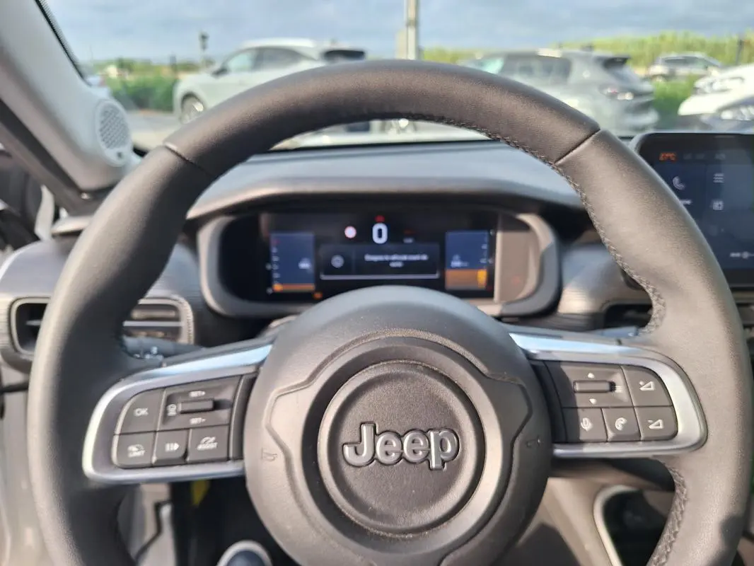 Vue rapprochée du volant Jeep Avenger blanc 2025, avec commandes intégrées et tableau de bord numérique en arrière-plan.