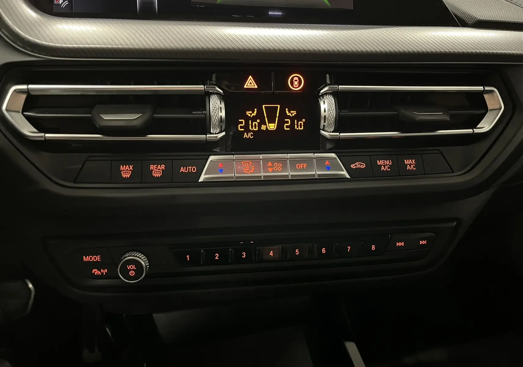 Vue rapprochée du tableau de bord noir de la BMW Série 1 F40 118dA, mettant en valeur les commandes de climatisation et audio rétroéclairées.