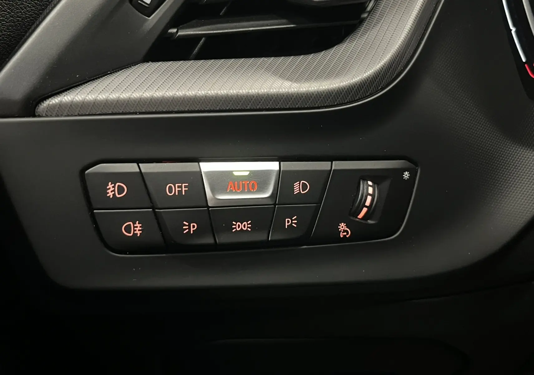 Gros plan sur les commandes d’éclairage avec réglage automatique et molette de luminosité, intérieur noir de BMW Série 1 F40.