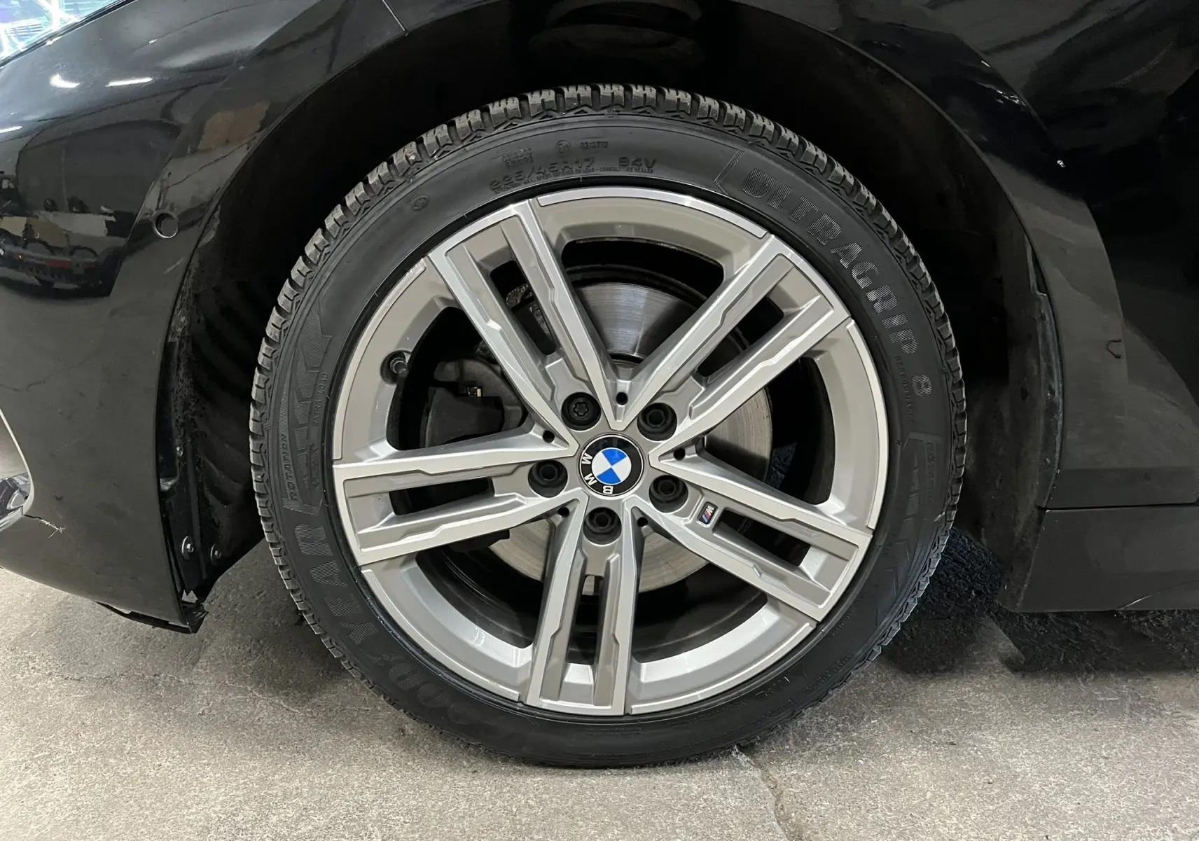 Gros plan sur la roue avant droite d’une BMW Série 1 noire métallisée avec jante alliage M sport à cinq branches doubles.