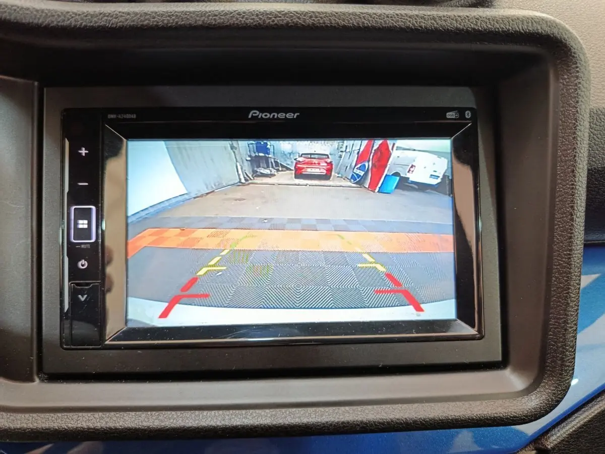 Écran de caméra de recul montrant l'arrière d'un véhicule blanc dans un garage, avec repères de guidage colorés.
