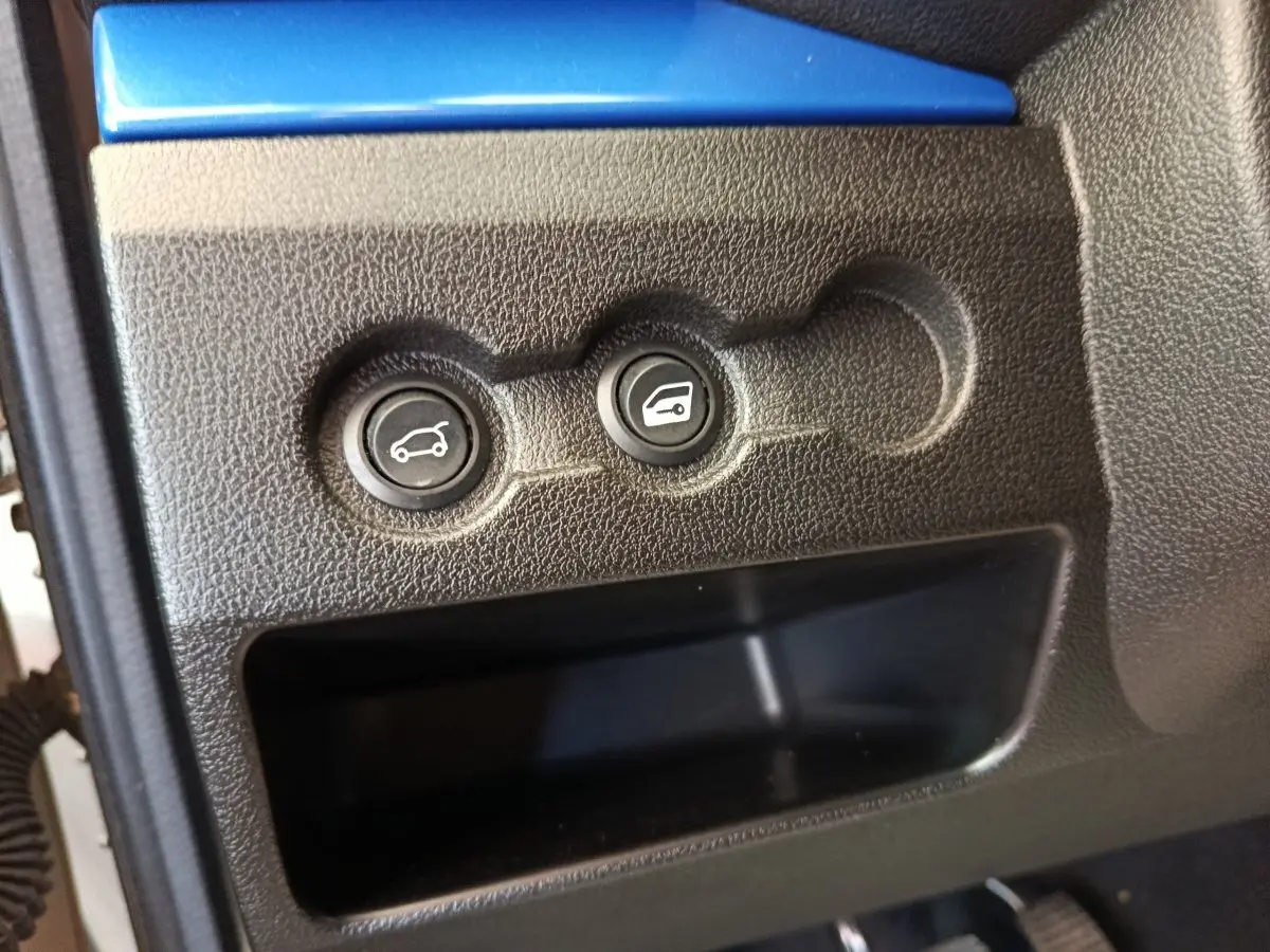 Gros plan sur les boutons d'ouverture du coffre et du capot d'une Aixam Ambition 0.5 City Coupe GTI blanche.