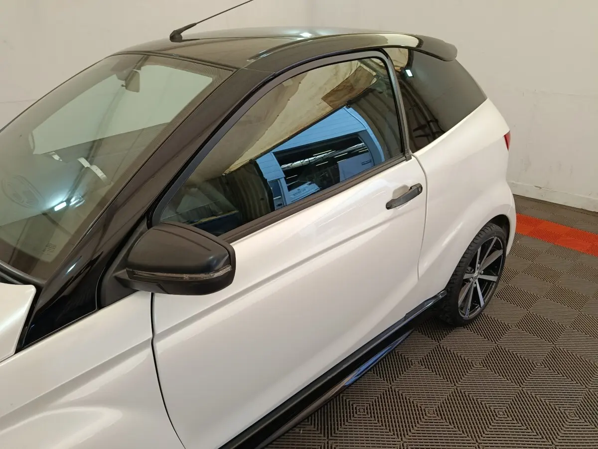Vue côté gauche rapprochée de l'AIXAM AMBITION 0.5 CITY COUPE GTI blanche avec toit noir et rétroviseur conducteur noir.